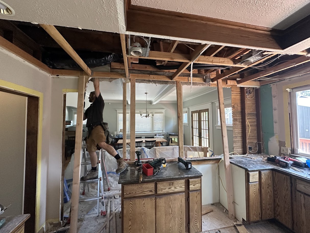 Kitchen wall removal in progress with worker on ladder at Forsyth home